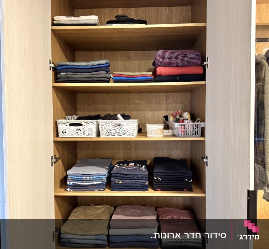 ארון בגדים מסודר עם מדפים, בגדים מקופלים וסלים.